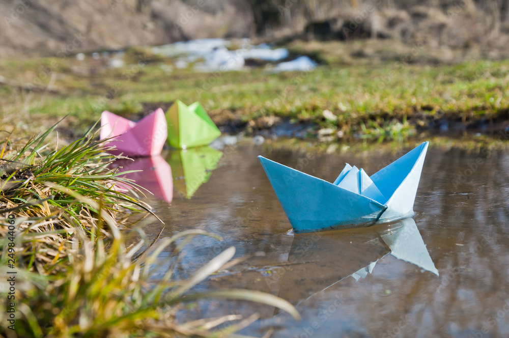 Colored paper boats float in the early spring puddles