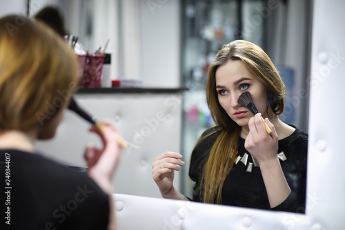 A young girl does make-up in a beauty salon. The girl in front of the mirror is making up. Beauty saloon.