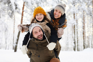 Portrait of playful happy family in winter forest looking at camera and smiling, copy space