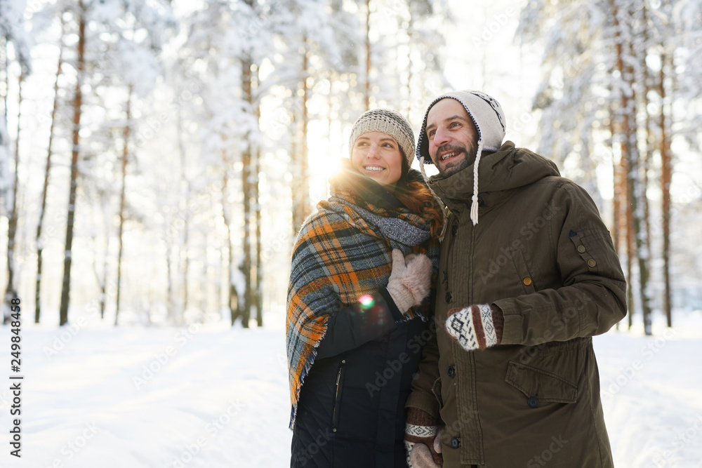 Waist up portrait of happy couple embracing in winter forest looking away dreamily, copy space Waist up portrait of happy couple embracing in winter forest looking away dreamily, copy space