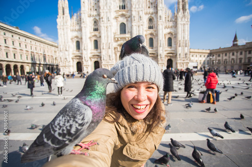 Italy, excursion and travel concept - young funny woman taking selfie with pigeons in front of cathedral Duomo in Milan