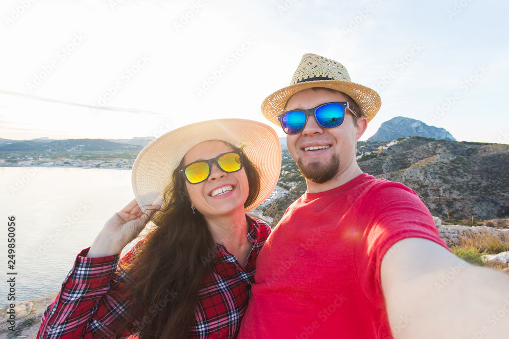 Travel, vacation and holiday concept - Pretty young woman and her handsome boyfriend in straw hats make selfie