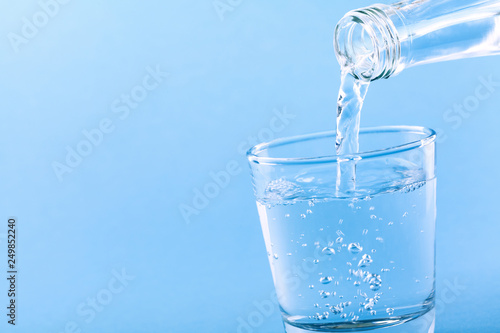 Fresh drinking water pouring into glass against blue background.