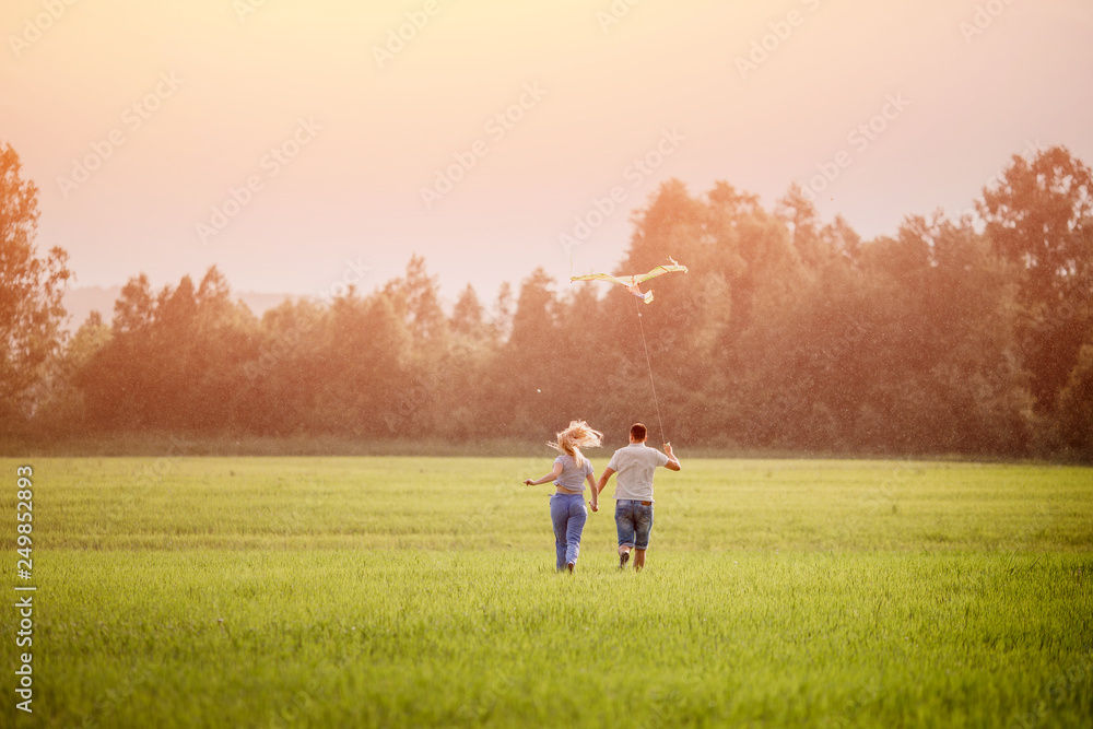 Loving couple runs for hands holding field in rain with kite, rear view. Concept family, freedom Loving couple runs for hands holding field in rain with kite, rear view. Concept family, freedom