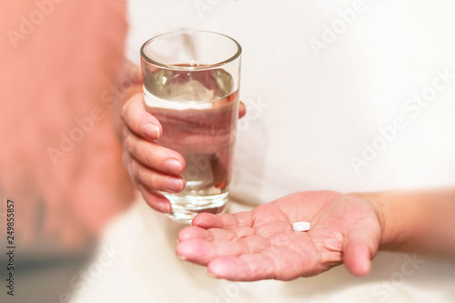 old hands are holding pills and a glass of water, medicine for an elderly woman, to drink a pill