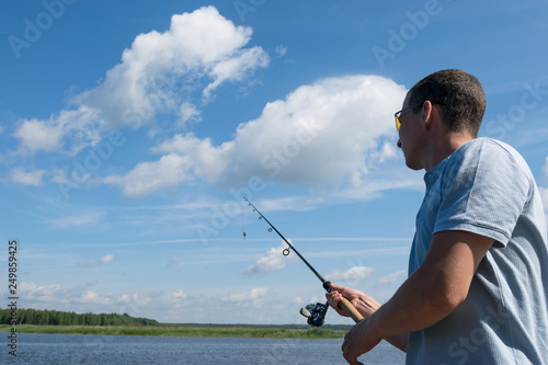 man holds spinning in his hand for fishing against the blue sky