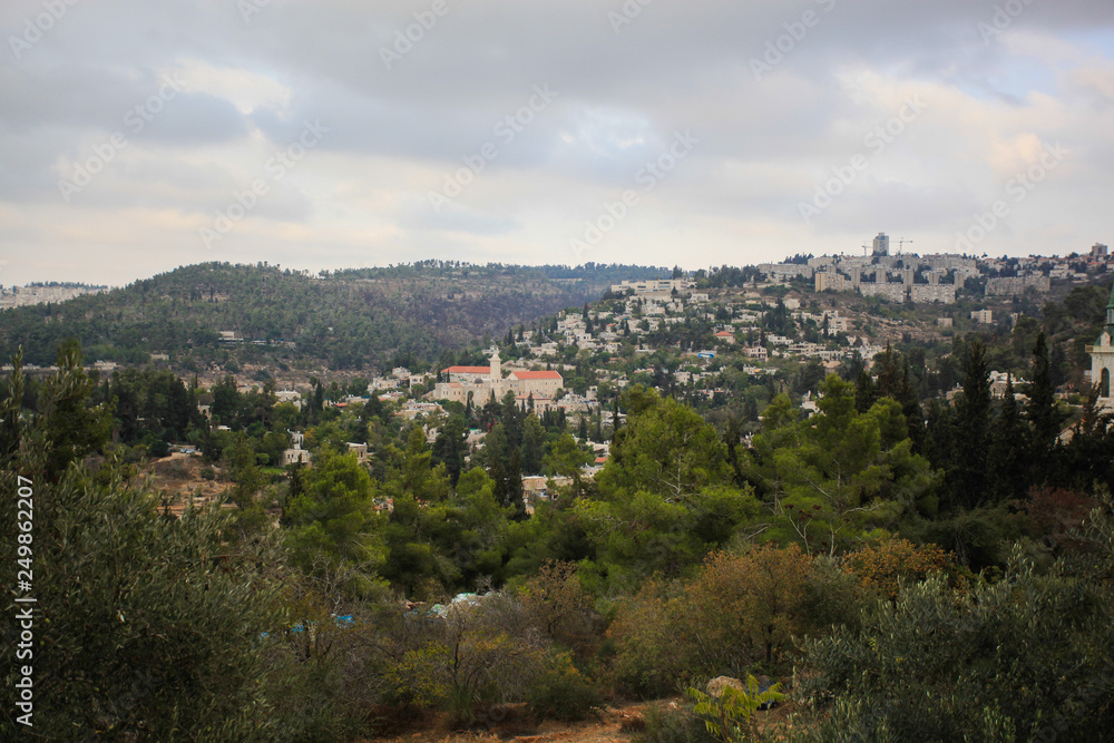 Green hills of Jerusalem with different buildings. Orthodox church and home. Trees and shrubs