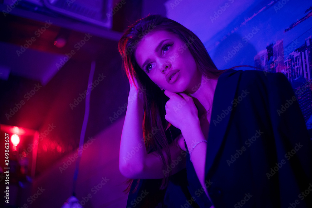Fashion portrait of young elegant girl. Beautiful brunette woman in neon light. Underwear, jacket shows a bare tummy. Colored background, studio shot