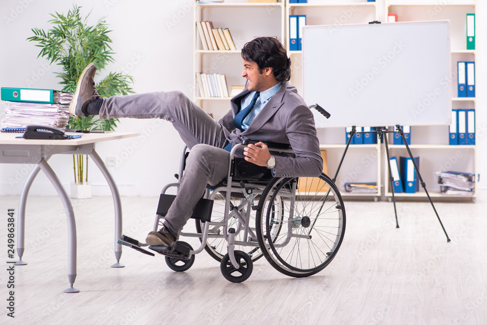 Young handsome employee in wheelchair at the office Young handsome employee in wheelchair at the office