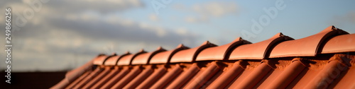 glänzend rote Dachziegel Pfanne vom Dachdecker Handwerker im Sonnenschein vor dunklem Hintergrund