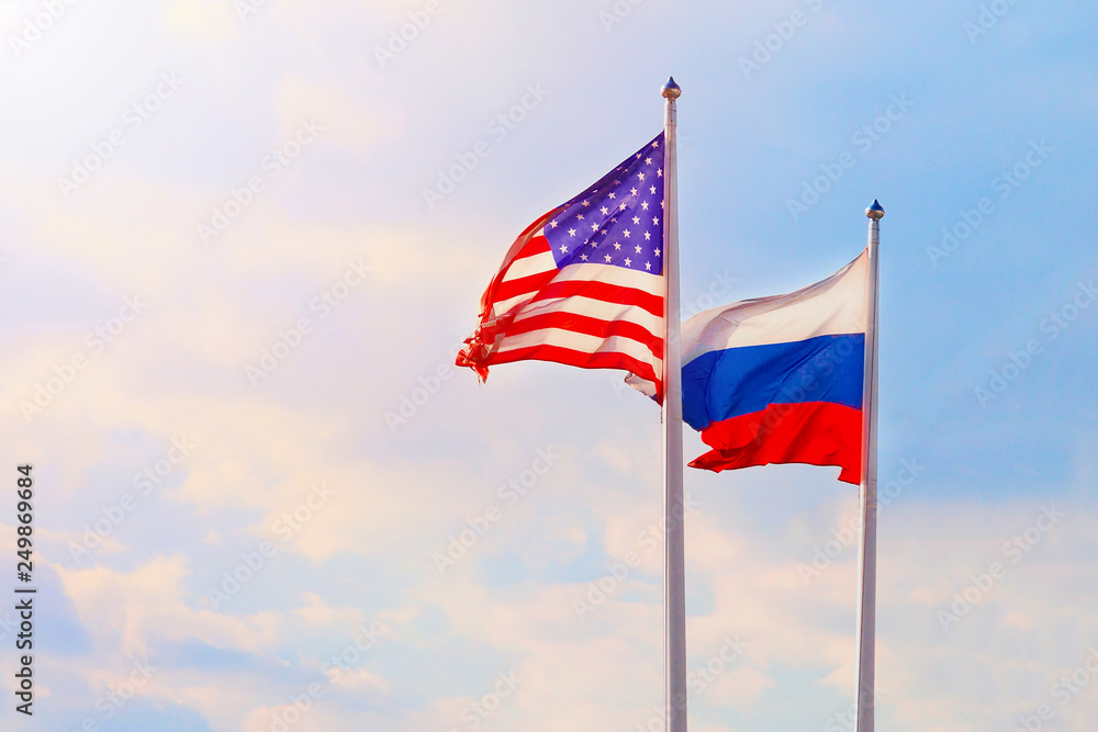 Russian Federation and United States of America flags on a blue sky background. Sanctions and confrontation concept. Free space.