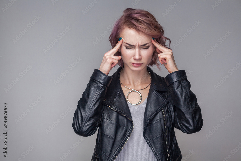 Headache. Portrait of woman with short hairstyle and makeup in casual style black leather jacket standing holding her painful head and closed eyes. indoor studio shot, isolated on grey background. Headache. Portrait of woman with short hairstyle and makeup in casual style black leather jacket standing holding her painful head and closed eyes. indoor studio shot, isolated on grey background.
