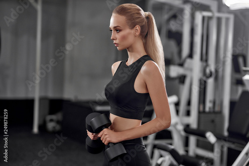 Motivated blonde raising dumbbells in gym.