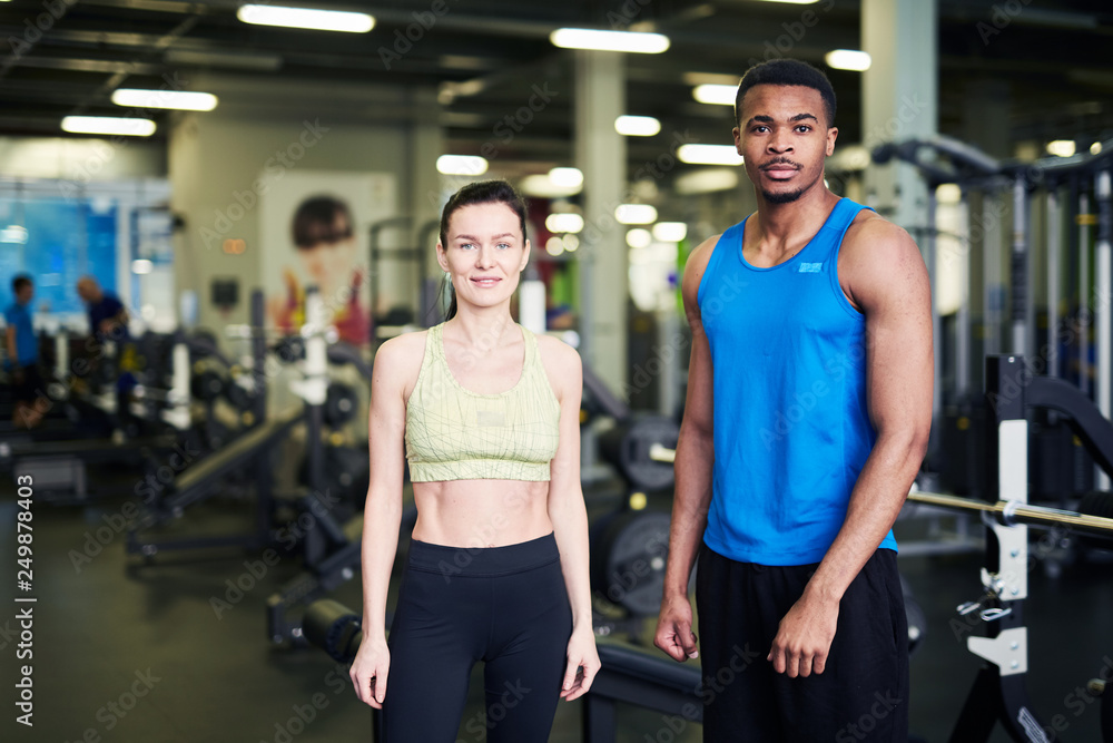 Two young active professionals in sportswear looking at you in contemporary fitness center Two young active professionals in sportswear looking at you in contemporary fitness center