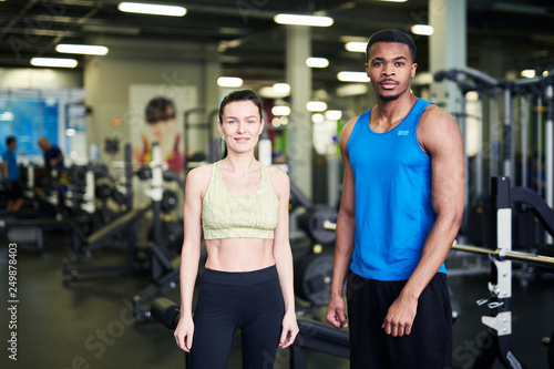 Two young active professionals in sportswear looking at you in contemporary fitness center