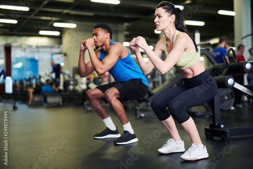 Young active man and woman standing on the floor with their knees and elbows bent while exercising in gym