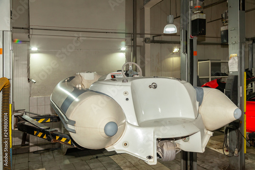 A small white rubber motorboat raised on a car lift for cleaning and repairs in a vehicle repair and maintenance workshop