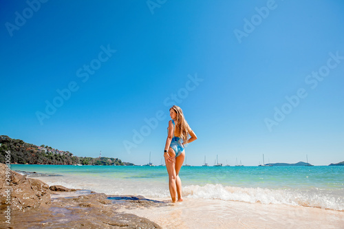 Beautiful young woman with long hair in a blue swimsuit standing back in the sea and relax on the beach on Phuket, Thailand