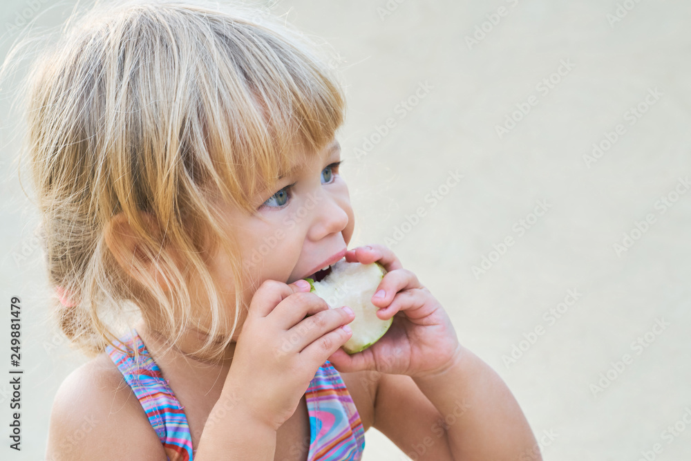 Cute adorable toddler girl eating fresh pear sitting on the beach. Cute adorable toddler girl eating fresh pear sitting on the beach.