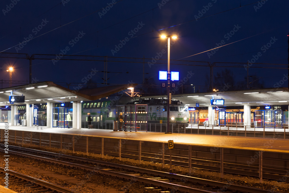 KOUVOLA, FINLAND - NOVEMBER 8, 2018: Long exposure photo. Train on the station at night. Blurred passengers with travel bags walking and staying on the platform.
