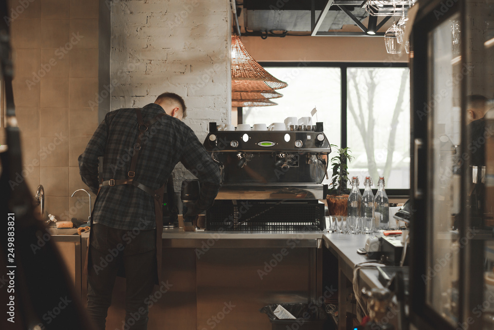 Portrait of a barista on the back at work near a coffee machine. Owner of a cafe and a coffee machine. Work of a barista in a cozy restaurant. Barista cooks the coffee at the atmospheric own cafe. Portrait of a barista on the back at work near a coffee machine. Owner of a cafe and a coffee machine. Work of a barista in a cozy restaurant. Barista cooks the coffee at the atmospheric own cafe.