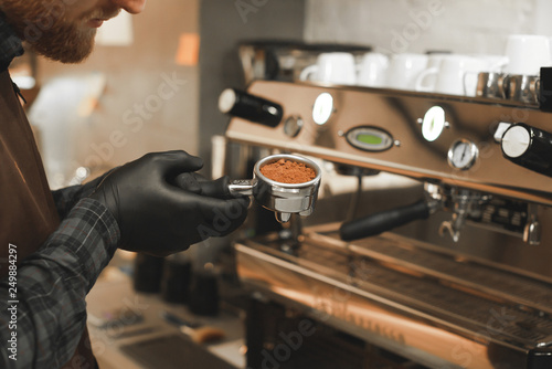 Close up photo of male barista holding portafilter at the coffee machine at the coffee shop. Barista s hands holding a holder with roasted coffee at the cafe. Preparing coffee concept.