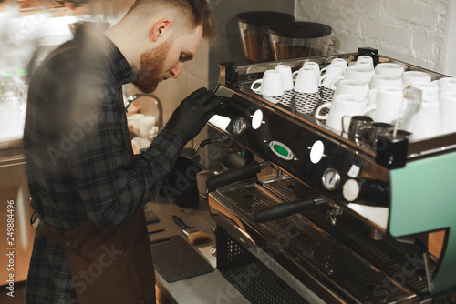 Concentrated barista is preparing coffee at coffee machine. Bearded cafe owner is focused on making delicious coffee drink in a coffee shop.