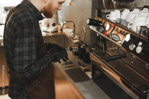 Close up photo of bearded barista holding portafilter at the coffee machine at the coffee shop. Barista's hands holding a holder with roasted coffee at the cafe. Coffee concept.