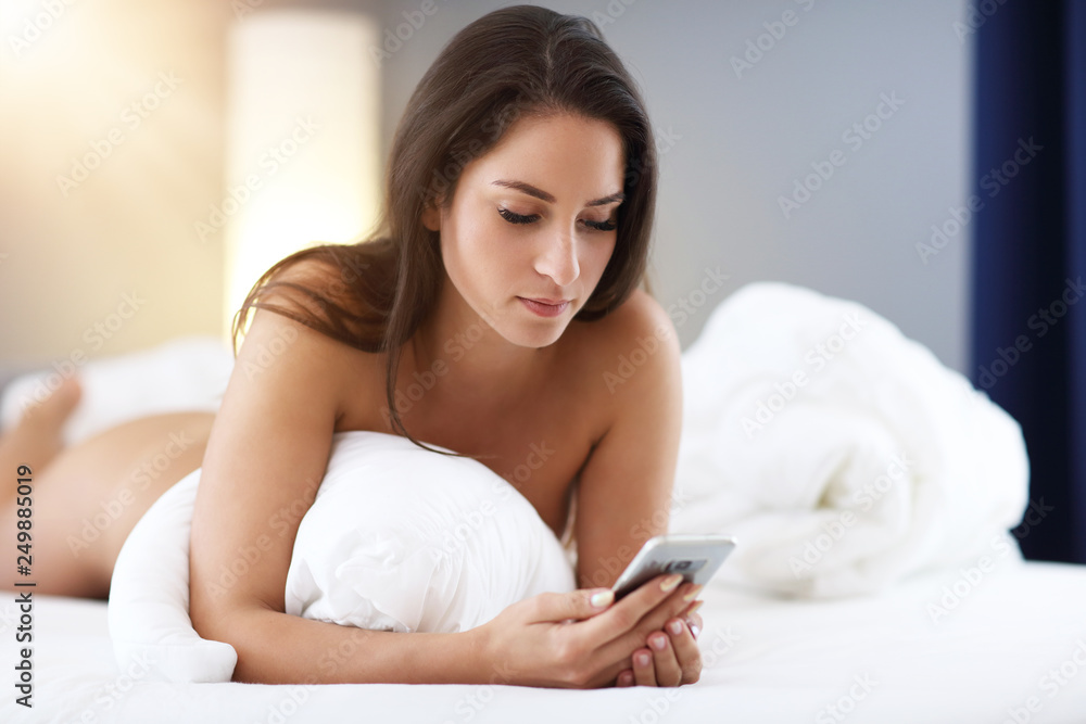 Young beautiful woman resting in bed with smartphone Young beautiful woman resting in bed with smartphone