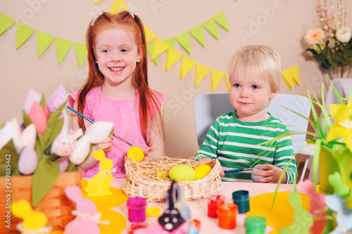 children - a little boy and a girl are preparing for the celebration of Easter. Brother and sister paint eggs on the background of the Easter decor