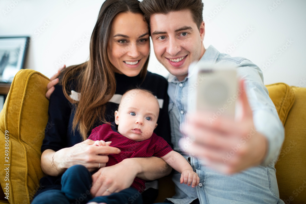 Family Sitting On Sofa At Home Posing For Selfie On Mobile Phone Family Sitting On Sofa At Home Posing For Selfie On Mobile Phone