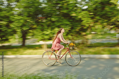 Fototapeta Naklejka Na Ścianę i Meble -  young woman in a dress rides a bike in a summer park
