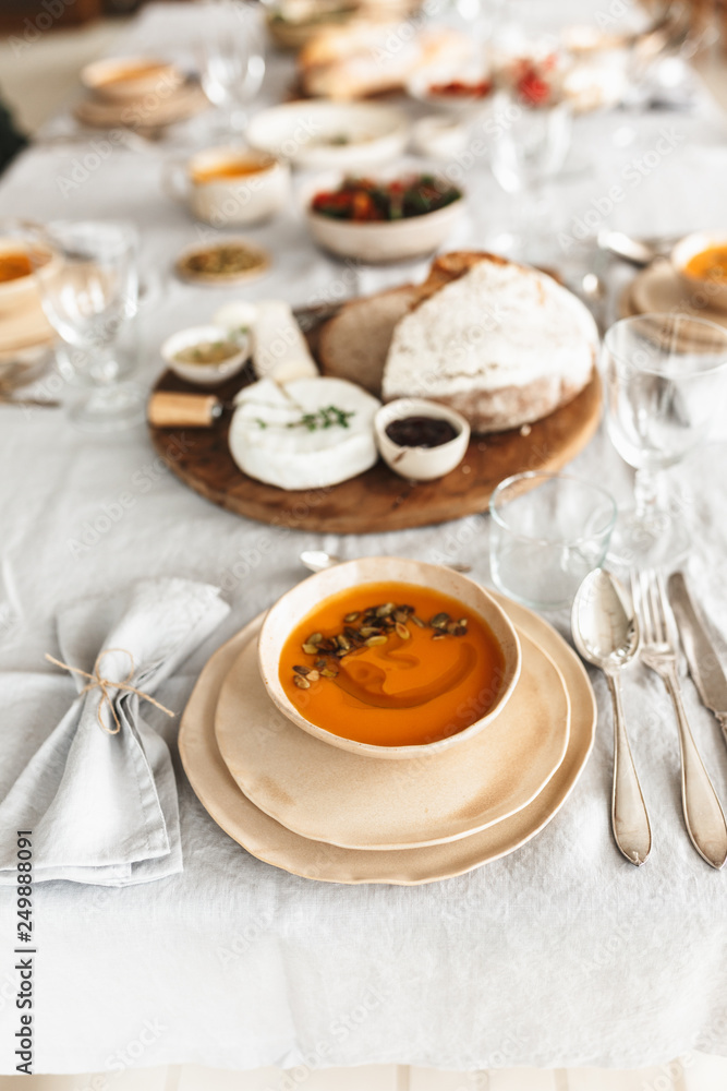 Close up bowl of pumpkin cream soup and fresh bread with cheese on wood board on white table in cozy cafe Close up bowl of pumpkin cream soup and fresh bread with cheese on wood board on white table in cozy cafe