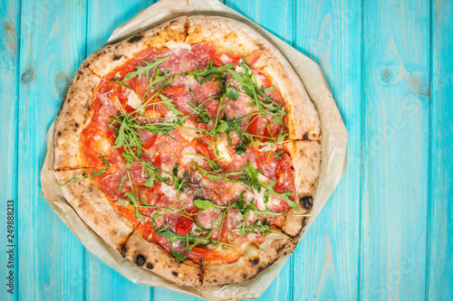 Pizza with prosciutto, arugula and parmesan on blue wooden background. Top view.