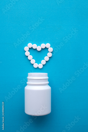 Pills, tablets in the shape of a heart and a white bottle on a blue background.