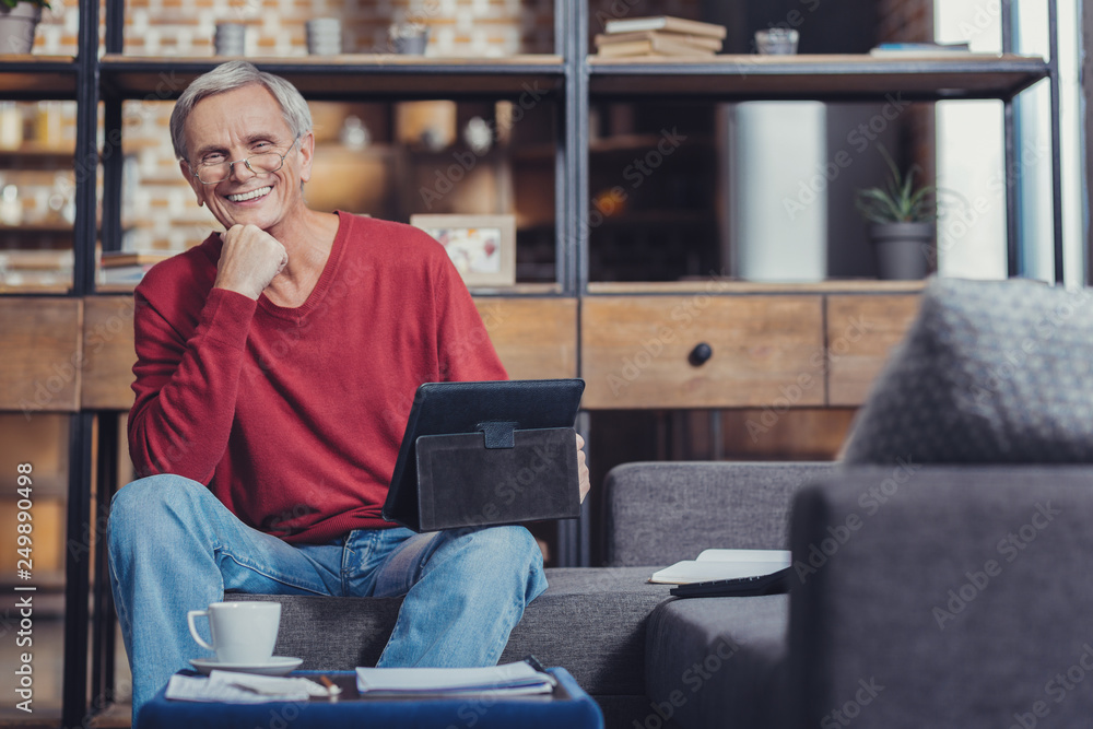 Obraz premium Positive pensioner smiling while sitting with a tablet
