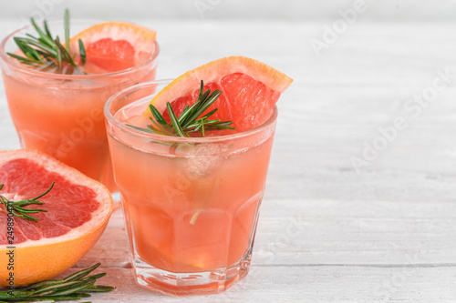 grapefruit cocktails in glasses with rosemary and ice on white background. Healthy citrus summer drink