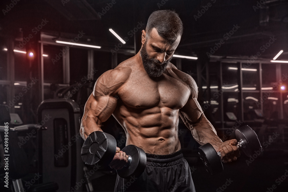 Muscular man working out in gym doing exercises with dumbbells, strong male naked torso abs