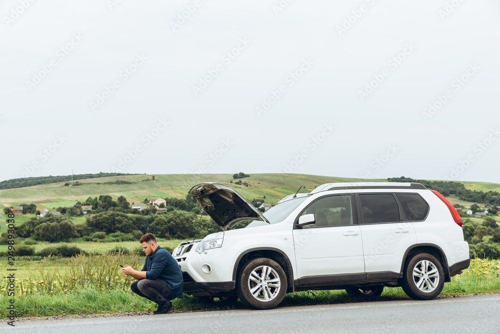 man sitting near broken car with phone, looking for help man sitting near broken car with phone, looking for help