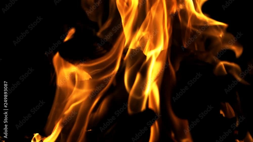 Black logs inside the bright flame burning at night on the dark background. Red flame surging up. Close-up Black logs inside the bright flame burning at night on the dark background. Red flame surging up. Close-up