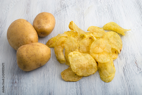 Chips with raw potatoes on white wooden background
