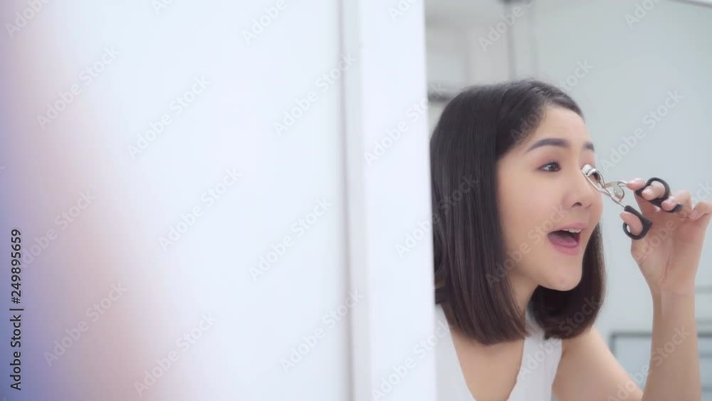 Beautiful Asian woman using eyelash curler makeup in front mirror, Happy female using beauty cosmetics to improve herself ready to working in bedroom at home. Lifestyle women relax at home concept. Beautiful Asian woman using eyelash curler makeup in front mirror, Happy female using beauty cosmetics to improve herself ready to working in bedroom at home. Lifestyle women relax at home concept.