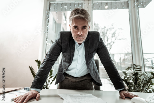Tall grey-haired adult manager in eyeglasses looking irritated