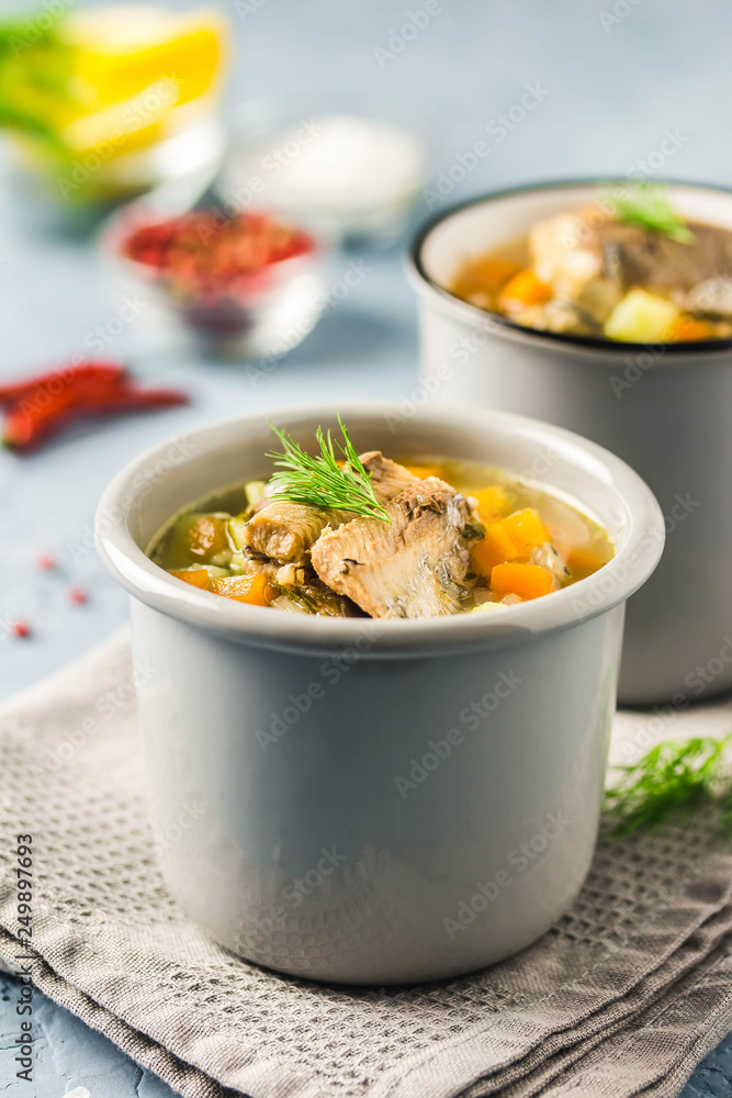Fish soup in mugs with fresh herbs and lemon. Selective focus, space for text.