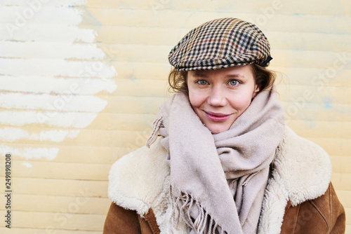 Portrait of a pretty hipster woman wearing hat outside smilling to camera. Yellow blicks wall behing, daylight. photo