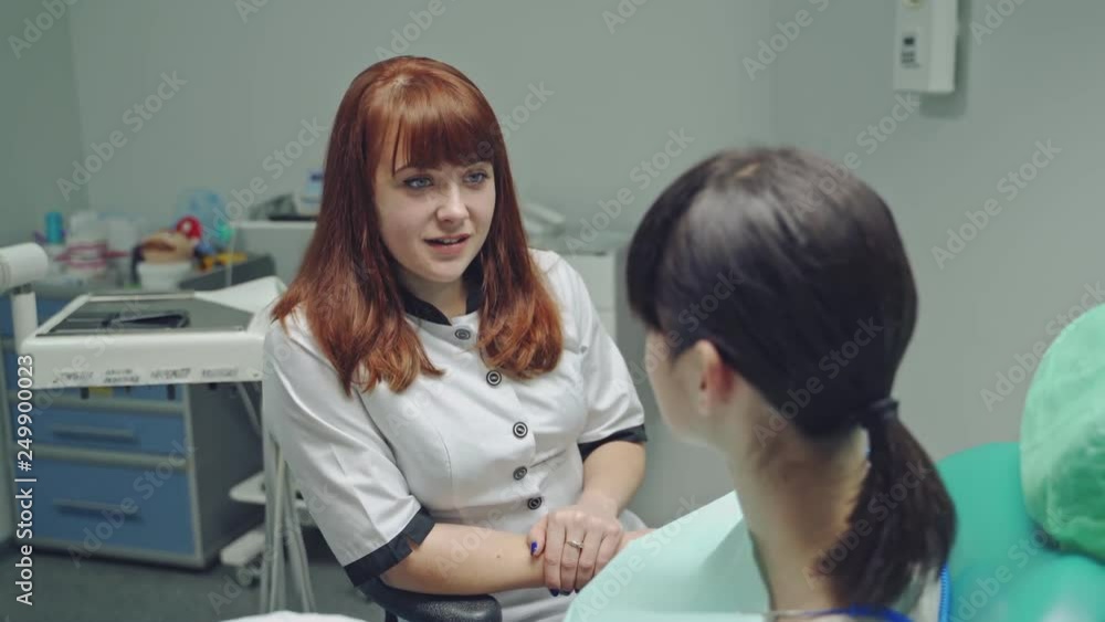 Happy dentist woman talking to a patient in a stomatology clinic. Female patient sitting in the chair and listens to the professional dentist doctor Happy dentist woman talking to a patient in a stomatology clinic. Female patient sitting in the chair and listens to the professional dentist doctor
