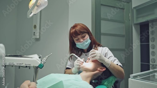 Beautiful dentist treating teeth to a woman patient in clinic over dental equipment background. Female professional doctor stomatologist at work.