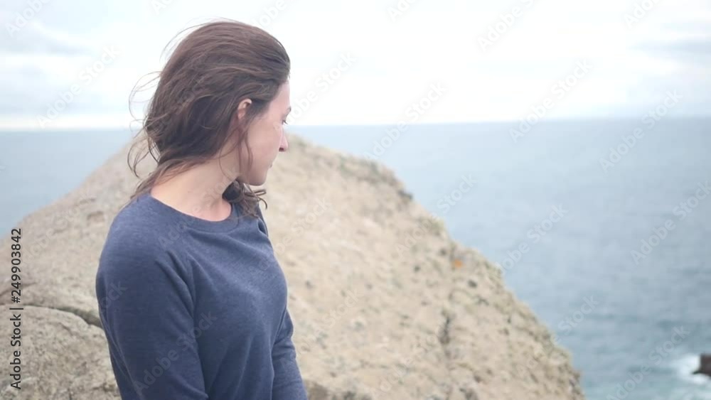Young woman standing on top of a cliff looking at the ocean Young woman standing on top of a cliff looking at the ocean
