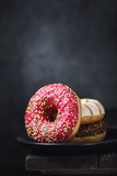Several donuts in a black ceramic plate on a wooden table with copy space