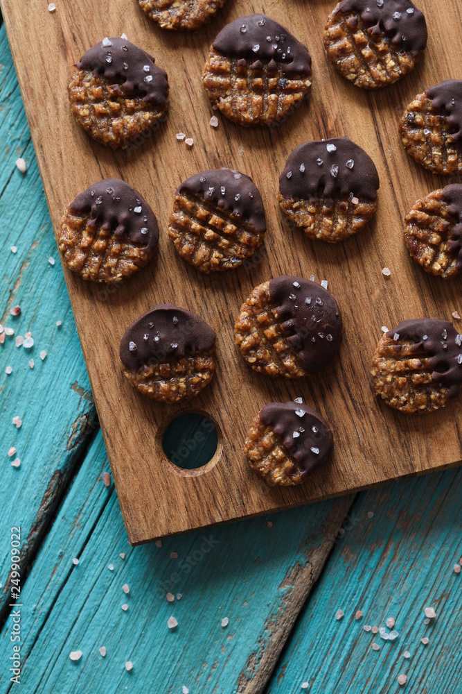 Fototapeta premium Raw vegan gluten and sugar free cookies with chocolate and salt served on wooden boards on blue background top view